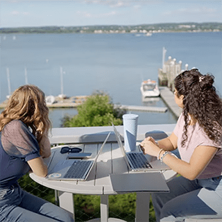 两个学生坐在帆船中心外的一张桌子旁，看着窗外的海湾